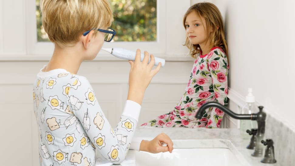A girl and a boy wearing pajamas in a bathroom brushing their teeth.