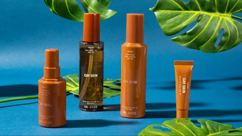 Four bottles and tubes of skincare against a blue background and foliage.