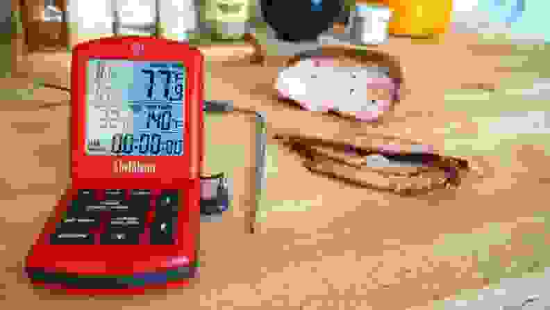 Probe thermometer sits on a wood counter next to sliced meat.