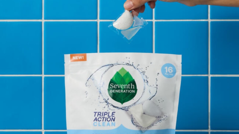 A dishwasher pack held above a bag of Seventh Generation dishwasher packs with a blue kitchen blacksplash