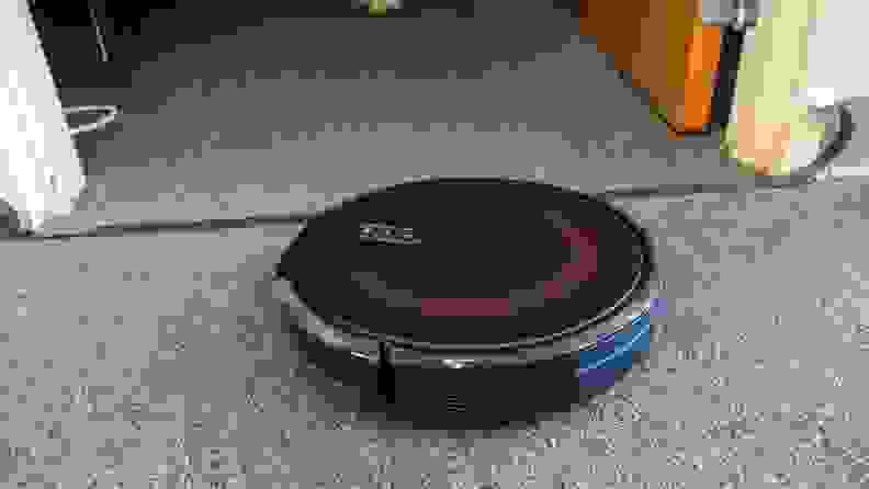 A Eufy Edge vacuum robot on a carpet in between a door.