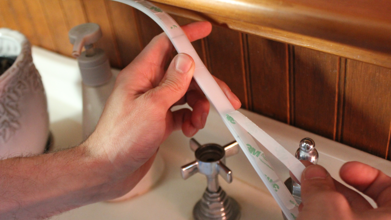 Person using hands to stick the GE Cync Lights underneath mirror.