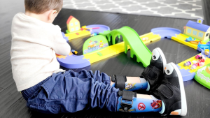 Child sitting on the floor playing with toys while wearing leg braces and the Ikiki adaptive shoe.