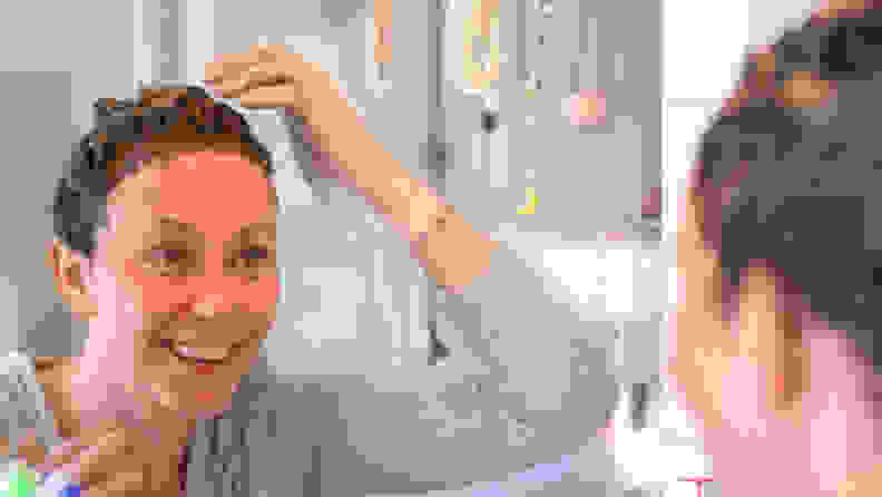A person looking into a mirror and smiling while applying hair dye all over their head.