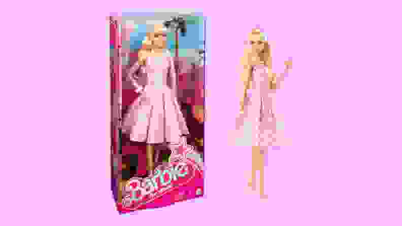 A Barbie in a pink gingham dress waves and stands next to another version of herself in her package.