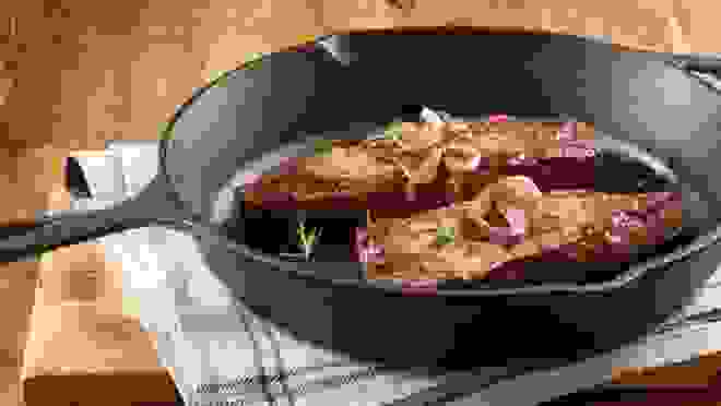 A cast iron skillet with seared meat on a kitchen table
