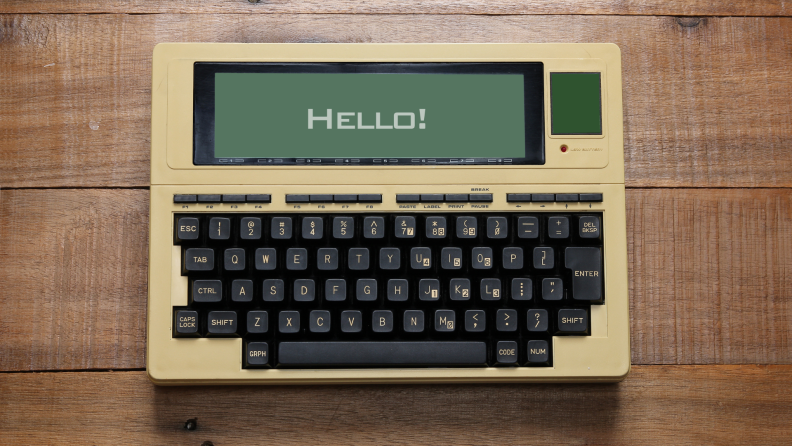 Retro keyboard with "Hello" displayed on screen, sitting on top of wooden surface.