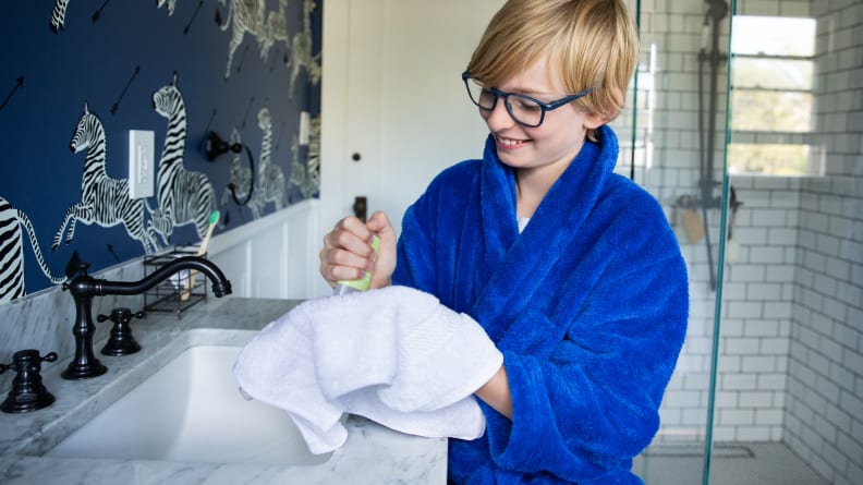 A boy in a bathrobe holding a washcloth