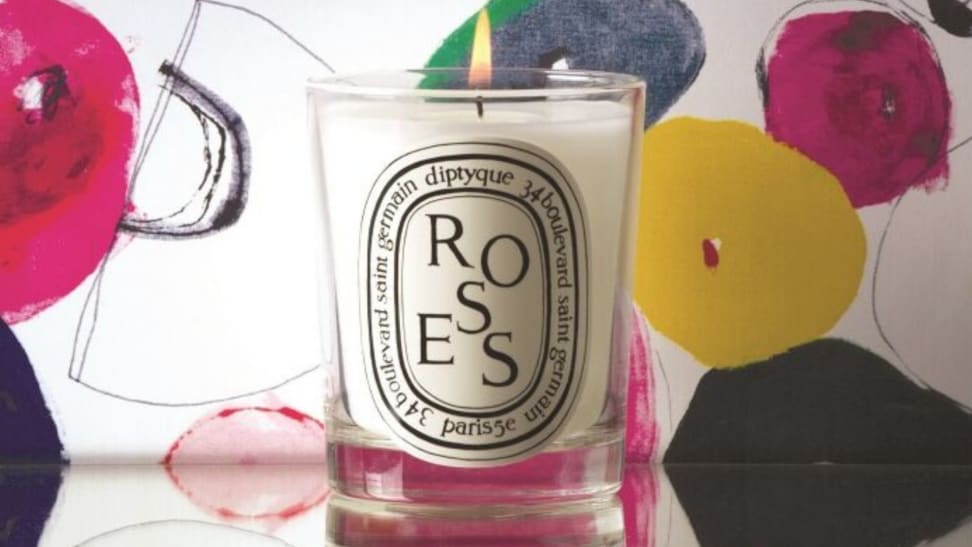A lit Diptyque candle sits on a table.