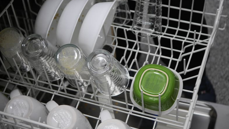 Top rack of dishwasher filled with bowls, coffee mugs, and glass cups.
