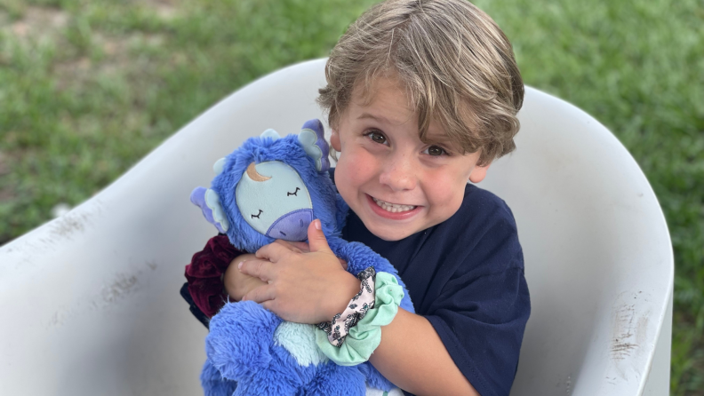Small child smiling outdoors while holding plush stuffed Slumberkins toy.