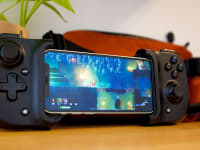 Razer's Kishi controller, with an iPhone docked in and playing Dead Cells, propped up against a plant and fanny pack.