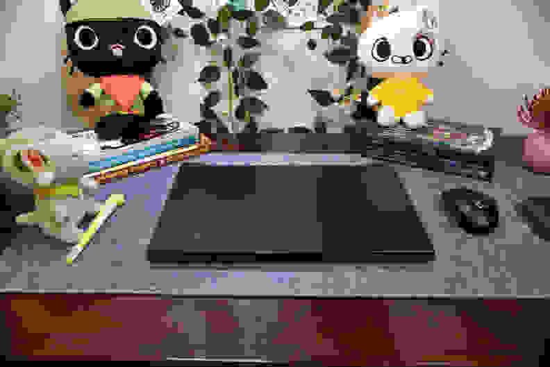 A closed, black laptop on top of a blue-gray mat with colorful plushies in the background