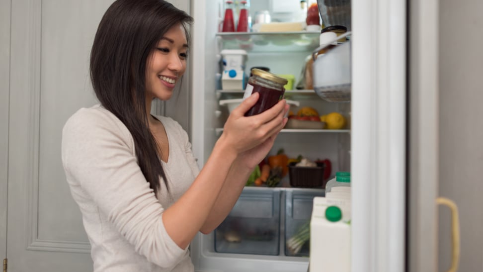 A person checking the label on a jar from the refrigerator.