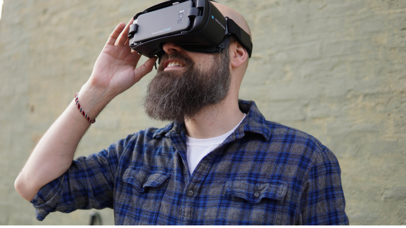 Sam Seavey shown standing in front of a white brick wall waring a VR headset.