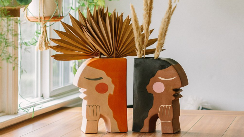 Two bookends designed like two women sitting on wooden table with fake plants inside