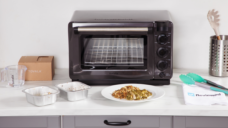 Tovala Smart Oven Pro on a white counter with food in front of it and tins and utensils on the counter.