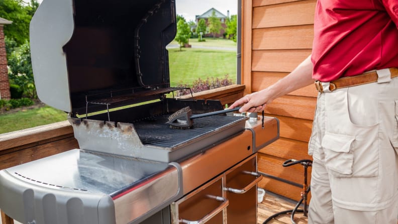 Person cleaning an open grill with a brush