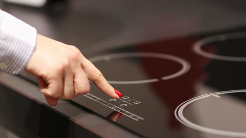 Female finger presses button on black induction stove top