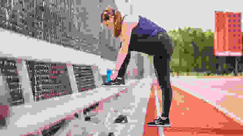 A woman tying her shoes on a bench at a track.