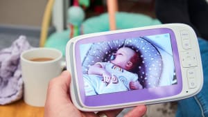 Person holding baby monitor in front of cup of coffee with sleeping baby monitor on screen.