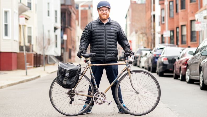 A man standing behind his bicycle in the road.