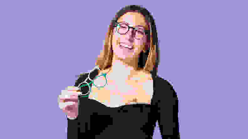 Woman wearing black shirt and smiling in pair of eyeglasses in front of purple background
