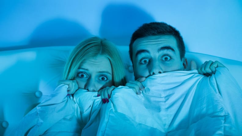 A couple hiding behind be sheets while watching a horror movie.