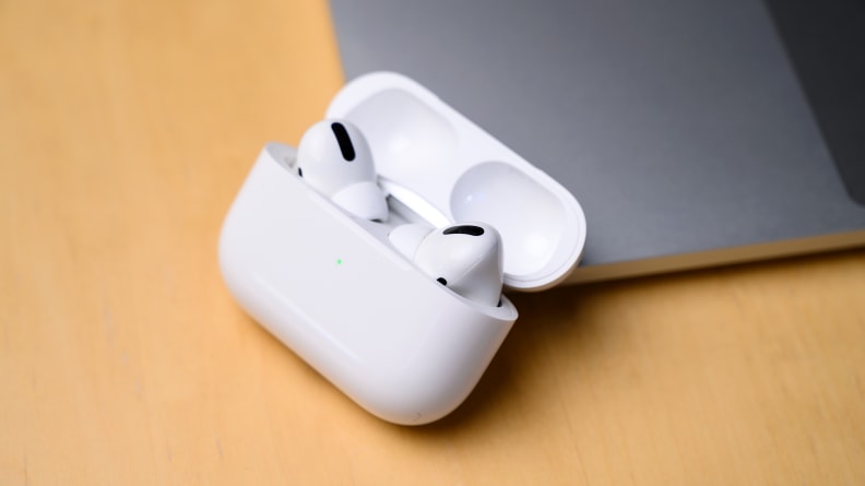 White-colored wireless earbuds lie on a beige desk next to a laptop.