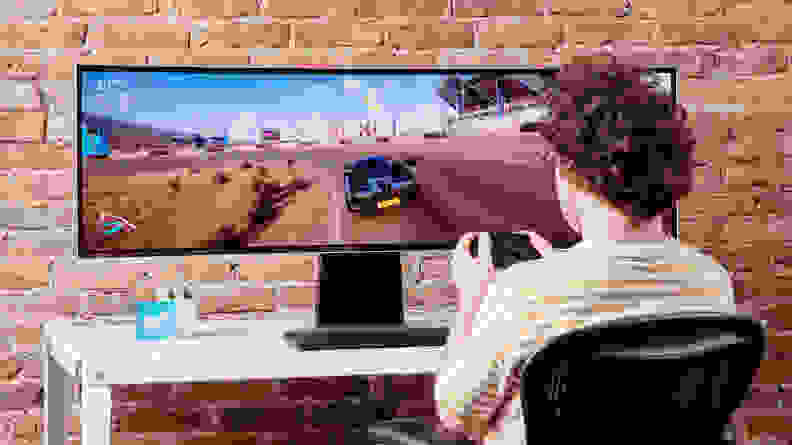 A person playing video games on the Samsung Odyssey OLED G9 on a brick background.