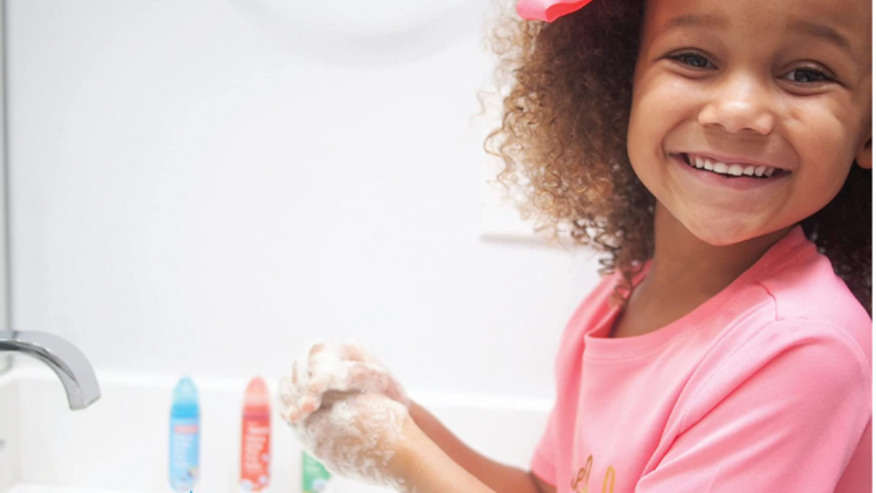 A child smiles as she washes her hands.