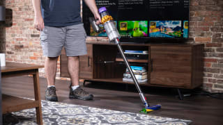 A person uses a Dyson V15 vacuum to clean the fllor