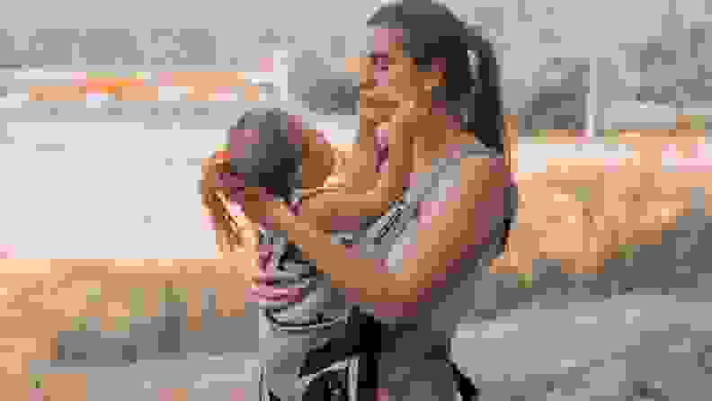 A mother plays with her child as she holds her in a carrier