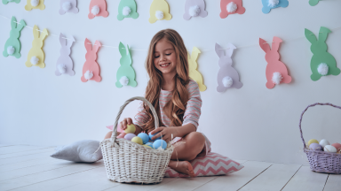 A girl sitting on the floor putting eggs in her Easter basket