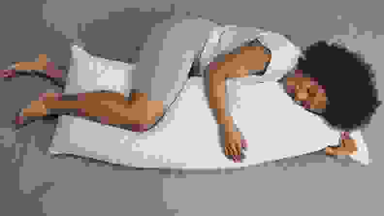 a woman curls up on her side with a body pillow