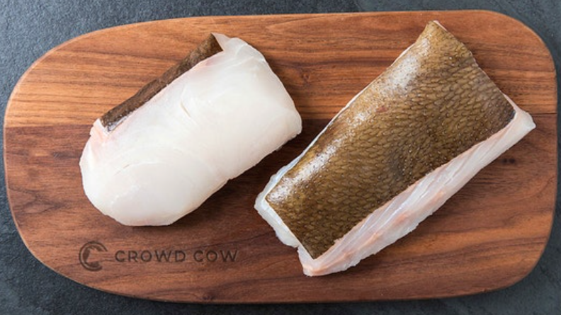 Two cuts of whitefish are displayed on a Crowd Cow carving board.