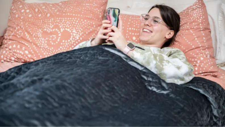 一个人躺在加重的毯子下看着他们的手机。