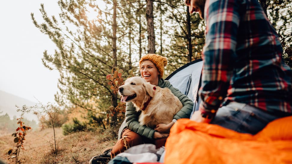 A woman holding a golden retriever sitting next to a man at a campsite.