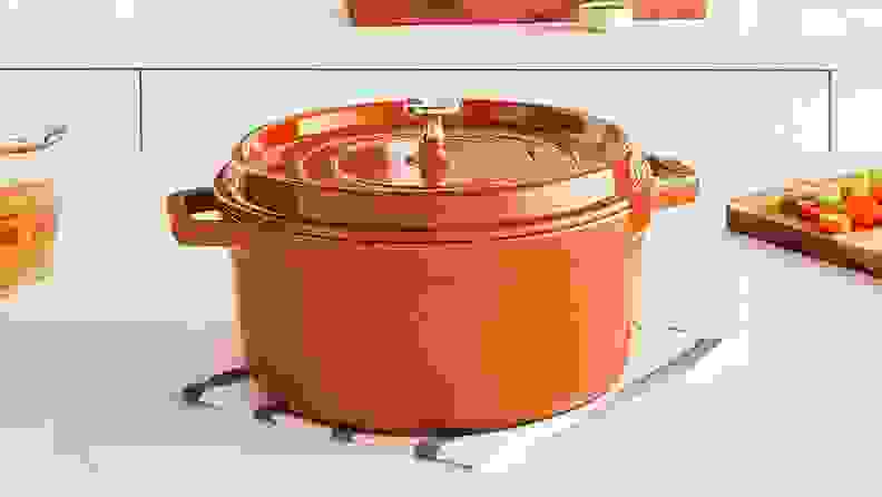 A bright orange Staub Dutch oven sits on a white kitchen counter.