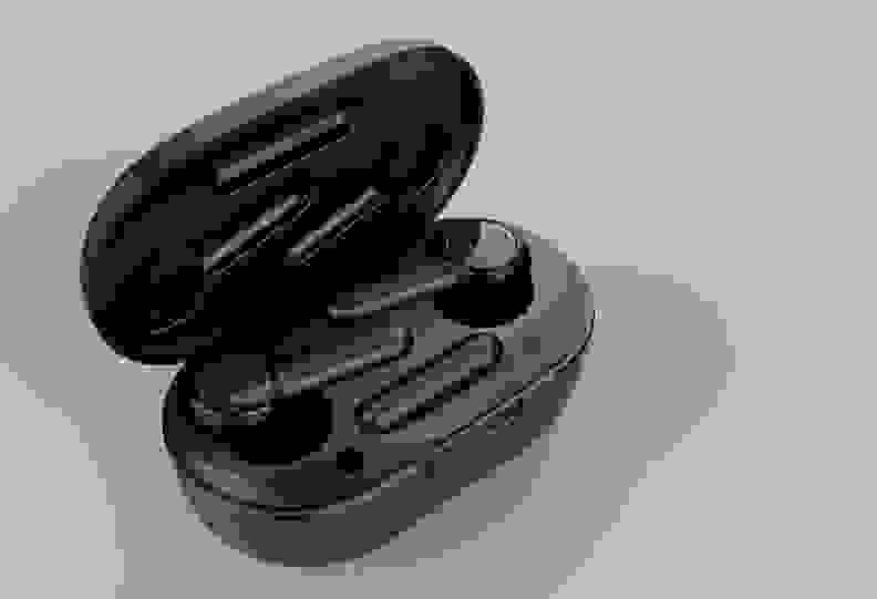 A pair of black, stick-style earbuds sit in an open black charging case with a grey background.