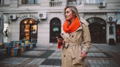 A woman wearing a trench coat with an orange sweater underneath.