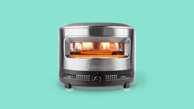 A stainless steel Solo Stove Prime Pi Pizza Oven with a fire inside the opening.