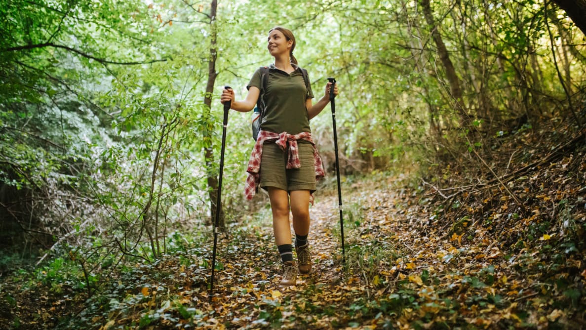 有个女孩拿着拐杖在树林里徒步。