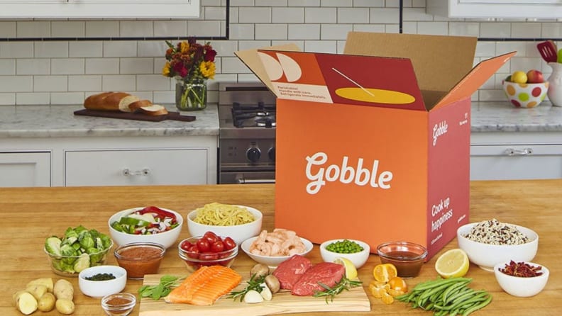 A Gobble meal kit box surrounded by fresh produce and other ingredients on a wooden kitchen countertop.