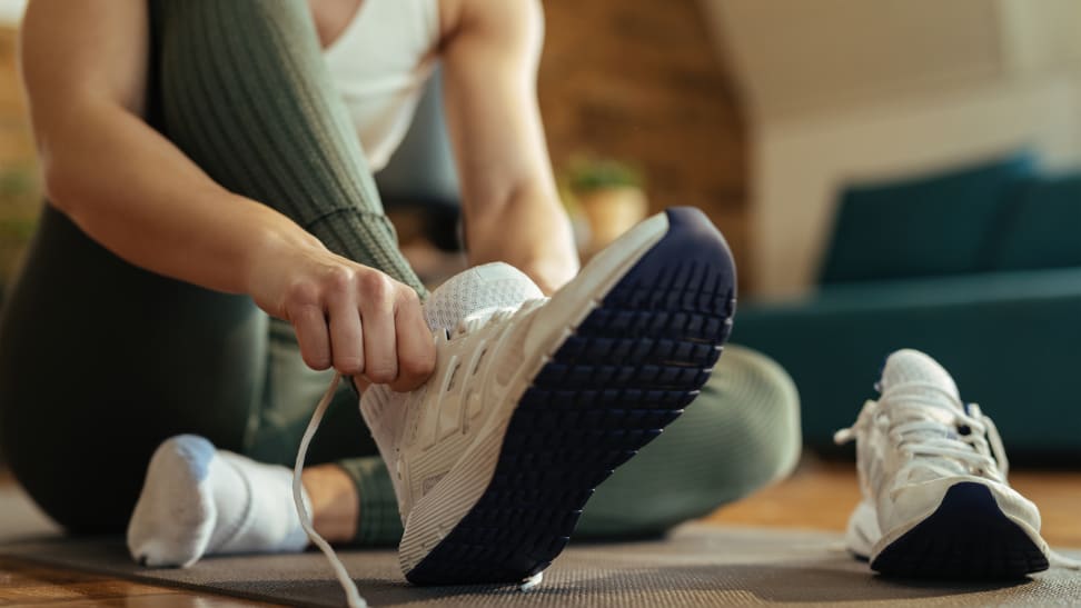 A woman putting a pair of white running shoes on.