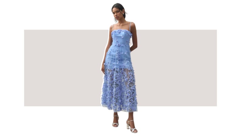 A model wearing a blue dress with applique flowers and sheer fabric throughout.