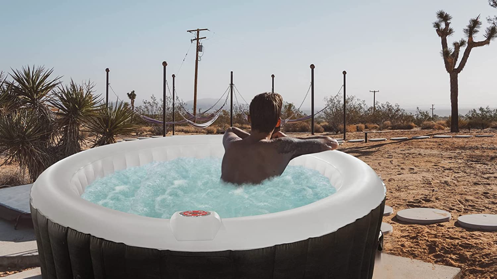 Photo of a model relaxing in an inflatable hot tub. A joshua tree is visible on the horizon.