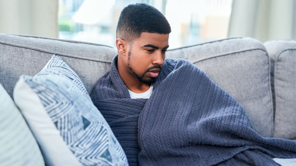 A person lounges on the couch wrapped in a blanket.