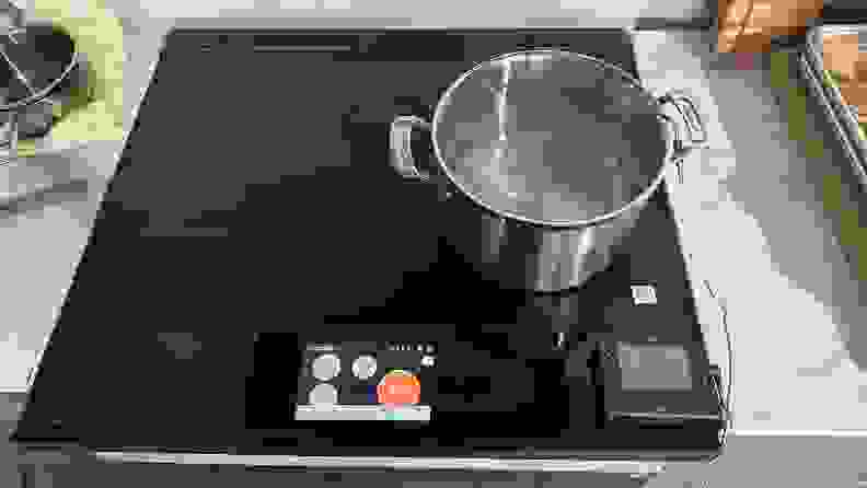 A pot of boiling water sits on the cooktop of the Samsung Bespoke NSI6DB990012AA Induction Range with a digital screen showing a red circle for the burner that's on.