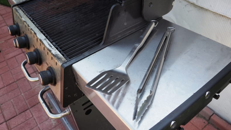 Grill tongs and spatula sit on a grill's side table.